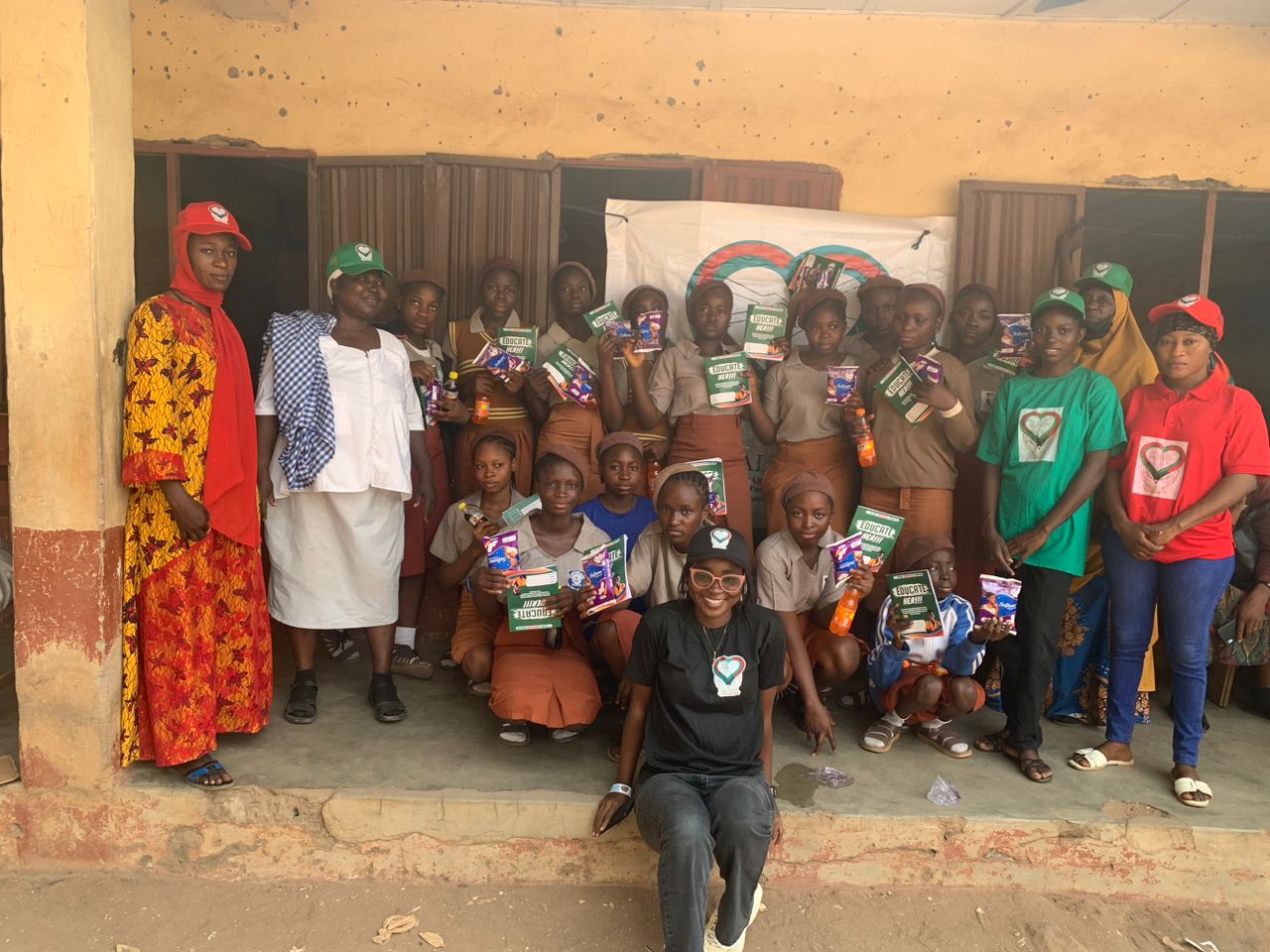 Schoolgirls and Halimat Humanitarian Foundation volunteers holding menstrual health packs during an outreach visit